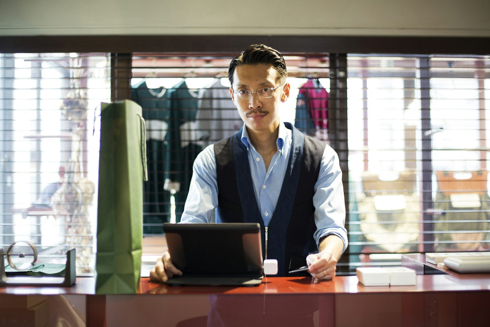 Japanese salesman standing at counter in clothing store, looking at digital tablet.